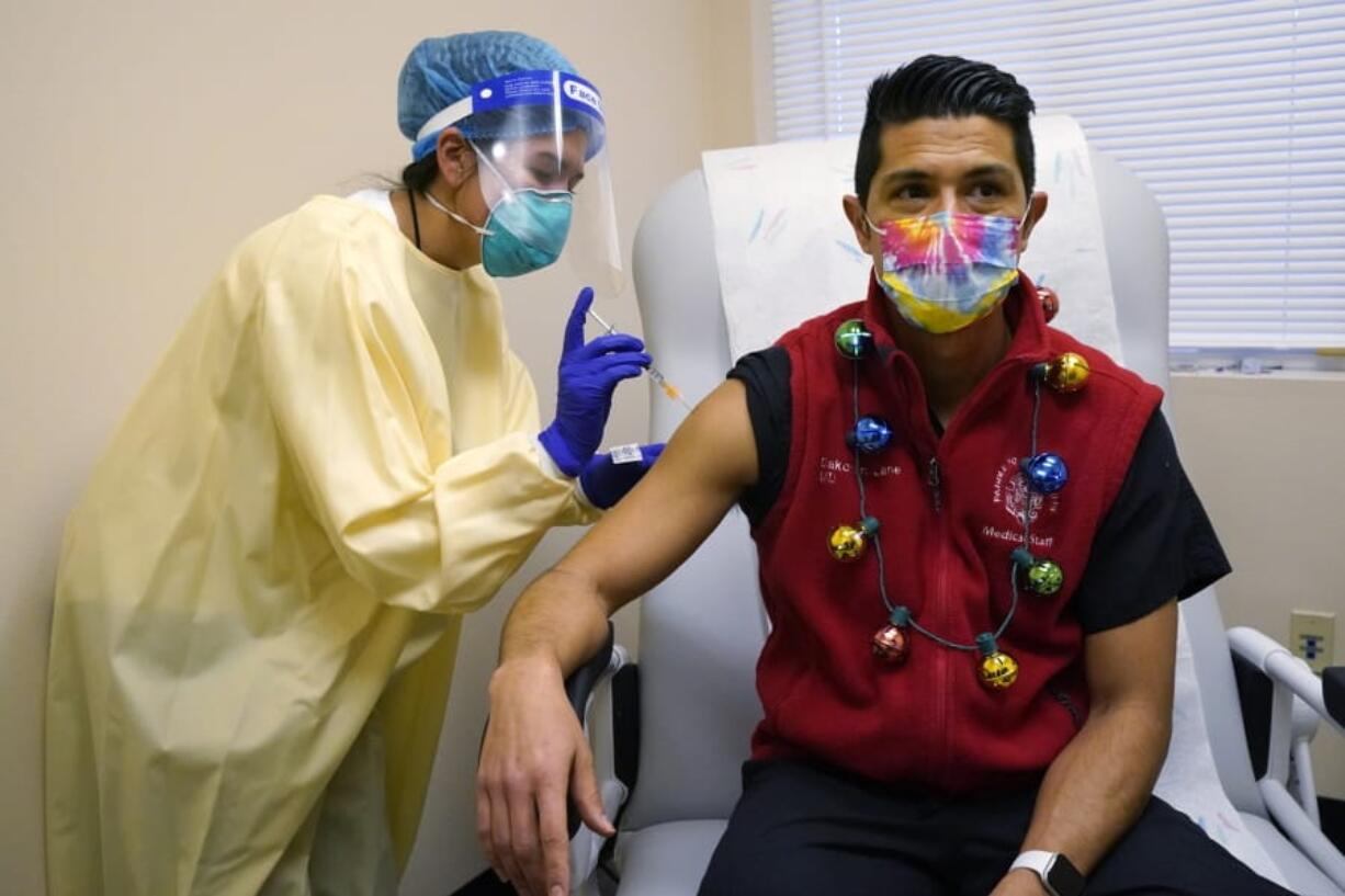 Dr. Dakotah Lane, a member of the Lummi Nation, right, receives a COVID-19 vaccination from registered nurse Alyssa Lane, his cousin, Thursday, Dec. 17, 2020, at the Chinook Clinic on the Lummi Reservation, near Bellingham, Wash. The Native American tribe began rationing its first 300 doses of vaccine as it fights surging cases with a shelter-in-place order.