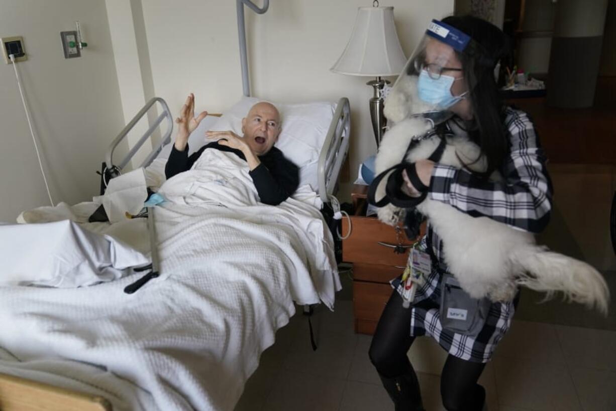 Jeff Philipson, 80, left, reacts on Dec. 9 as therapeutic activities staff member Kate DelPizzo arrives for a visit with Zeus, a bichon frise, at The Hebrew Home at Riverdale in New York. New dog recruits are helping to expand the nursing home&#039;s pet therapy program, giving residents and staff physical comfort while human visitors are still restricted because of the pandemic.