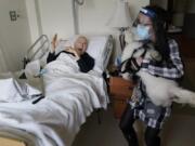 Jeff Philipson, 80, left, reacts on Dec. 9 as therapeutic activities staff member Kate DelPizzo arrives for a visit with Zeus, a bichon frise, at The Hebrew Home at Riverdale in New York. New dog recruits are helping to expand the nursing home&#039;s pet therapy program, giving residents and staff physical comfort while human visitors are still restricted because of the pandemic.