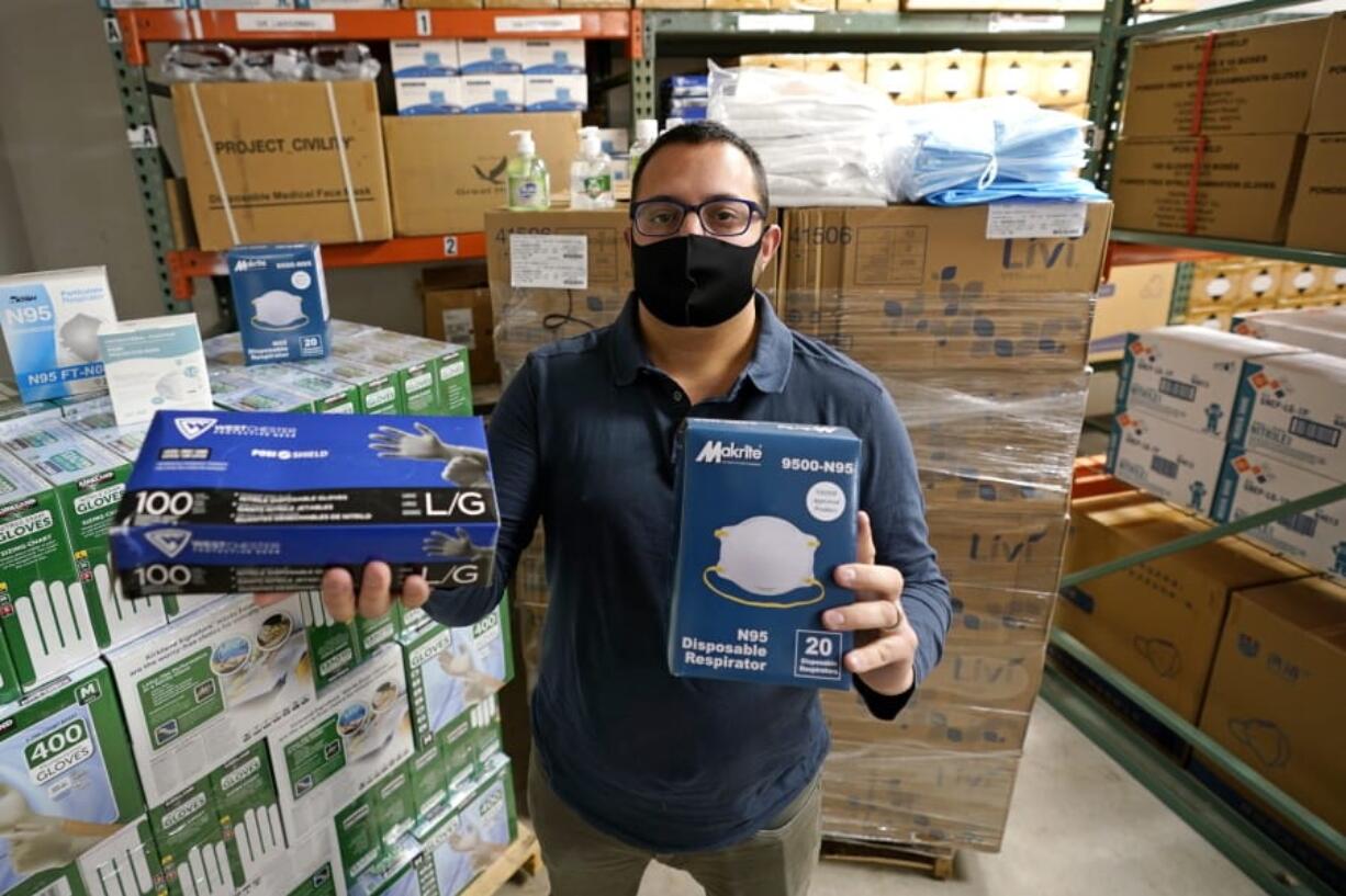 Ray Bellia holds up personal protective masks and gloves, used by medical and law enforcement professionals, in the warehouse of his Body Armor Outlet store, Wednesday, Dec. 9, 2020, in Salem, N.H. Bellia&#039;s store rapidly evolved into one of the nation&#039;s 20 largest suppliers of personal protective equipment to states this past spring, according to a nationwide analysis of state purchasing data by The Associated Press.