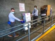 University of Washington Medical Center Montlake campus pharmacy administration resident Derek Pohlmeyer, left, and UWMC pharmacy director Michael Alwan transport a box containing Pfizer-BioNTech COVID-19 vaccines toward a waiting vehicle headed to the UW Medical Center&#039;s other hospital campuses on Monday, Dec. 14, 2020, in Seattle.