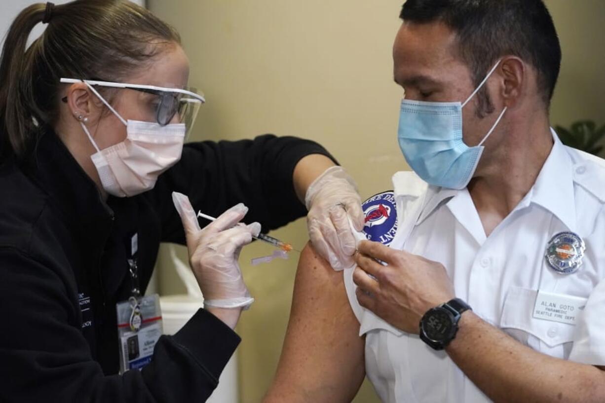 Seattle Fire Dept. paramedic Alan Goto, right, receives one of the first Pfizer-BioNTech COVID-19  vaccinations by registered nurse Allison Miller at UW Medicine, Tuesday, Dec. 15, 2020, in Seattle.