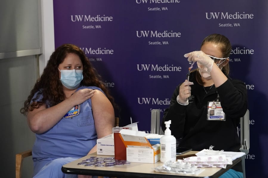 Amy Fry, left, a nurse in the COVID ICU at Harborview Medical Center, holds up her sleeve to receive the first Pfizer-BioNTech COVID-19 vaccination at UW Medicine from registered nurse Allison Miller, Tuesday, Dec. 15, 2020, in Seattle.