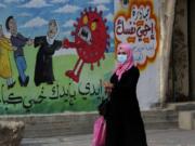 A woman walks past a mural encouraging the wearing of face masks amid the coronavirus pandemic, on the main road of Nusseirat refugee camp, central Gaza Strip, on Nov. 24, 2020. Arabic reads: &quot;protect yourself, together we protect the old.&quot; The prickly orb is on every news and medical site. It&#039;s all over TV and on flyers for COVID car cleaning.