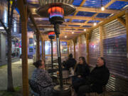 Heaters at the outdoor dining area of the Main Event in downtown Vancouver add warmth for customers Alyson Hilken, from left, Krissy Sadewasser and John Laughlin as they enjoy a happy hour drink.  At top, a sign informs customers of alternative dining options at Main Event.