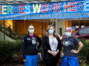 Melissa Glascock, from left, a respiratory therapist, Colette Reilly, a nurse manager, and Lisa Streissguth-Kasberg, a charge nurse, pose in front of a "Heroes Work Here" banner outside Legacy Salmon Creek Medical Center. Clark County hospitals have seen spikes in coronavirus patients this fall and winter.