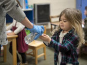 Parent helper Sarah Stowe gives Aurora Lund, 3, a pump of hand sanitizer following snack time on Tuesday at the Camas-Washougal Parent Co-Op preschool. All students received hand sanitizer after snack time before returning to coloring projects.