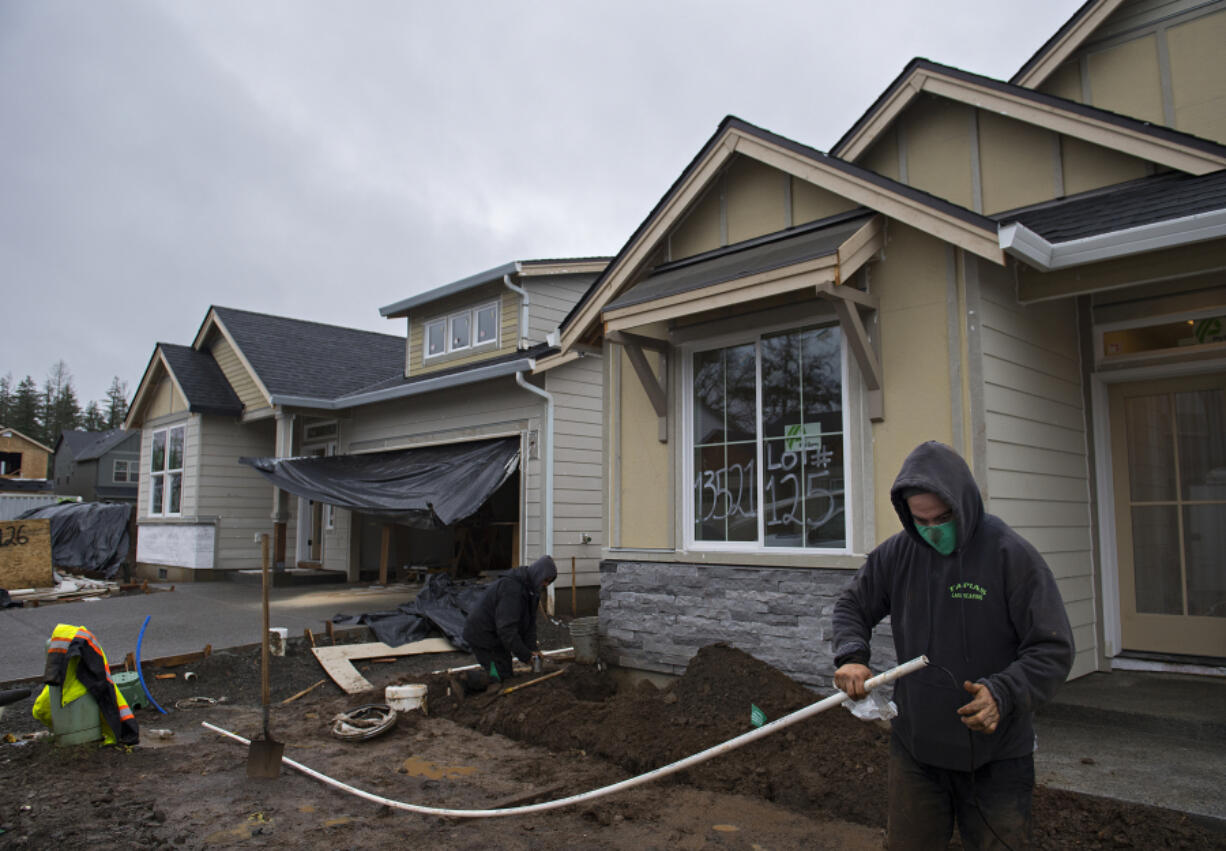 Marco Perez of Tapias Landscaping, right, works in the front yard of a home under construction in the Parker&#039;s Abby development in Vancouver on Tuesday. New home construction is booming in Vancouver, but the region still faces a housing supply crunch. Below, signs mark two homesites that have been sold at the Stonehaven development in Vancouver.