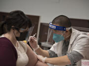 Homecare administrative assistant Ashley Hill, left, receives the COVID-19 vaccine from Jordan Tran of CVS Pharmacy at Touchmark at Fairway Village in Vancouver.