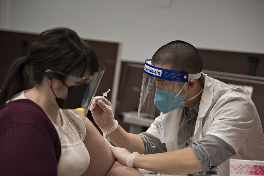 Homecare administrative assistant Ashley Hill, left, receives the COVID-19 vaccine from Jordan Tran of CVS Pharmacy at Touchmark at Fairway Village in Vancouver.