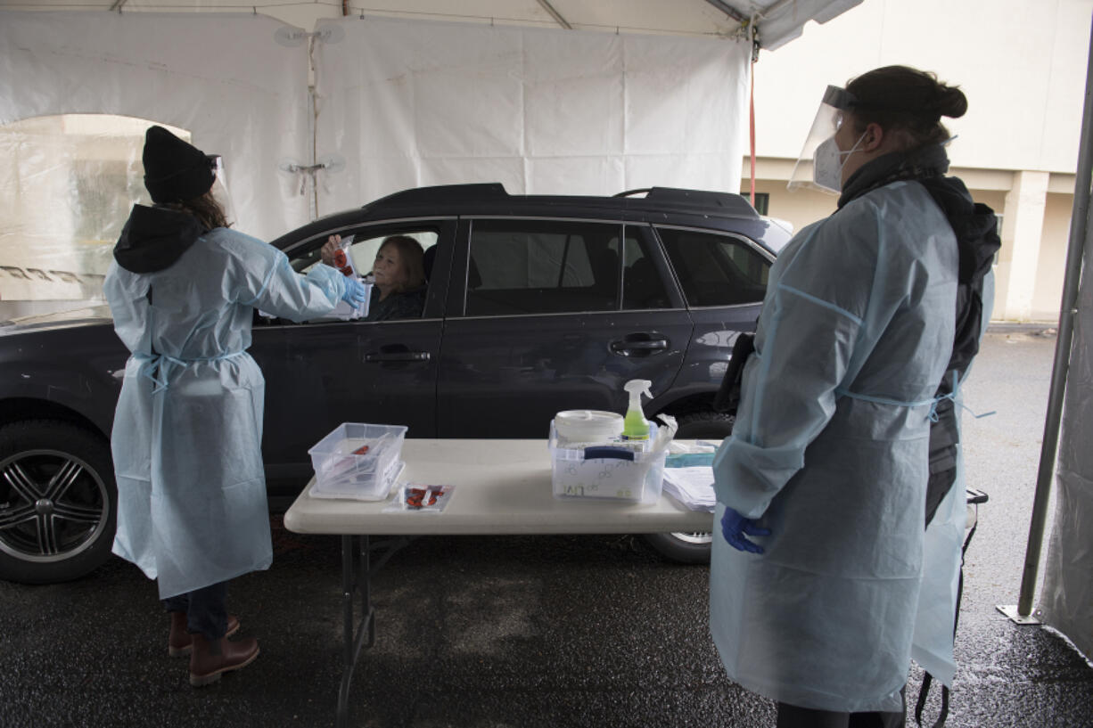 Allison Berhow of Northwest Staffing, left, collects a sample COVID-19 test from Vancouver Mayor Anne McEnerny-Ogle as Jenny Wilson of Vancouver&#039;s Parks and Recreation Department looks on during a practice run of the new COVID-19 testing site at Tower Mall on Monday afternoon. Officials said all sample tests collected on Jan. 11 would be safely discarded and not processed for results.