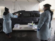 Allison Berhow of Northwest Staffing, left, collects a sample COVID-19 test from Vancouver Mayor Anne McEnerny-Ogle as Jenny Wilson of Vancouver&#039;s Parks and Recreation Department looks on during a practice run of the new COVID-19 testing site at Tower Mall on Monday afternoon. Officials said all sample tests collected on Jan. 11 would be safely discarded and not processed for results.