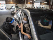 Kelly Nguyen of Safeway, left, gives a COVID-19 vaccination to Flor Bonura of Washougal as her husband, Thomas, snaps a photo with his smartphone at the Clark County Event Center at the Fairgrounds on Tuesday morning, January 26, 2021. Tuesday was the first day of mass vaccinations in Clark County, which are given by appointment only.