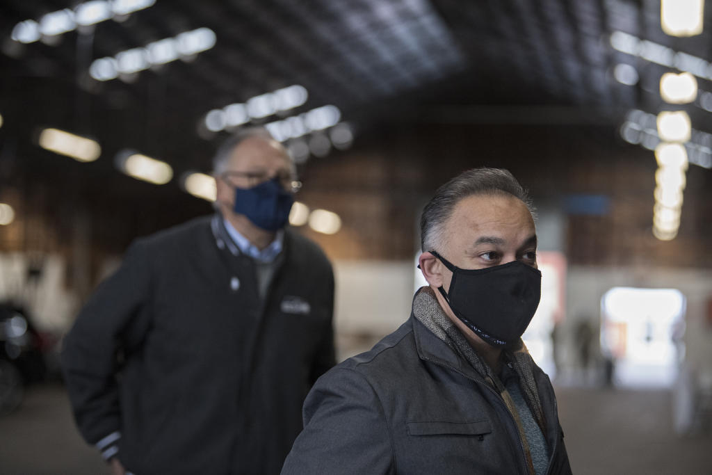 Gov. Jay Inslee, background left, listens as Washington Secretary of Health Dr. Umair Shah speaks to the media during a tour the COVID-19 mass vaccination site at the Clark County Fairgrounds on Thursday morning, January 28, 2021.