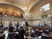 Senate members stand as a ceremonial presentation of colors is done virtually on a video screen above Monday, Jan. 11, 2021, at the Capitol in Olympia, Wash. Washington state's Legislature convened Monday under a large security presence because of concerns about efforts by armed groups who might try to disrupt the proceedings or occupy the Capitol, which is closed to the public due to the ongoing pandemic. (AP Photo/Ted S.