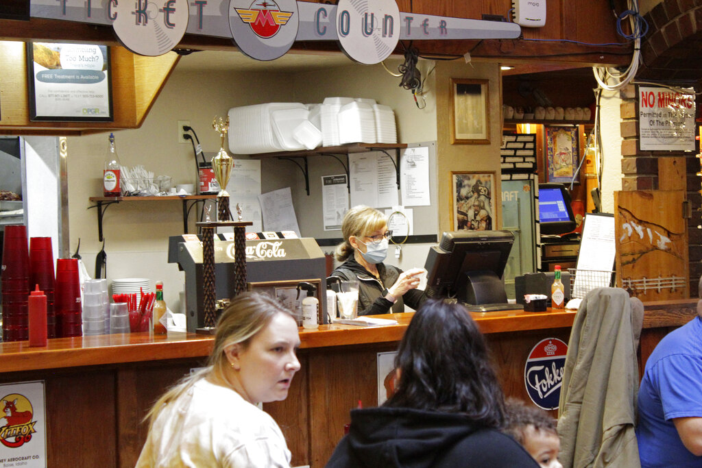 Restaurant co-owner Liz Mitchell works behind the bar at the Carver Hangar in Boring, Ore., on Jan. 6, 2021. As coronavirus deaths soar, a growing number of restaurants like Carver Hangar in states across the country are reopening in defiance of strict COVID-19 rules that have shut them down for indoor dining for weeks, or even months.