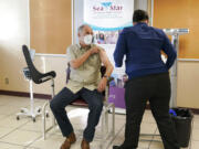 Washington Gov. Jay Inslee, left, smiles after he received the first shot of the Moderna COVID-19 vaccine, Friday, Jan. 22, 2021, from Elizabeth Smalley, right, a medical assistant at a Sea Mar Community Health Center in Olympia, Wash. Inslee's wife Trudi also received the first dose of the vaccine. (AP Photo/Ted S.