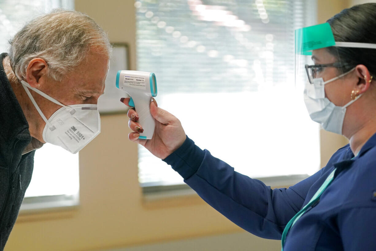 Washington Gov. Jay Inslee, left, has his temperature taken by Elizabeth Smalley, right, a medical assistant at a Sea Mar Community Health Center, before he received the first shot of the Moderna COVID-19 vaccine, Friday, Jan. 22, 2021, in Olympia, Wash. Inslee's wife Trudi also received the first dose of the vaccine. (AP Photo/Ted S.