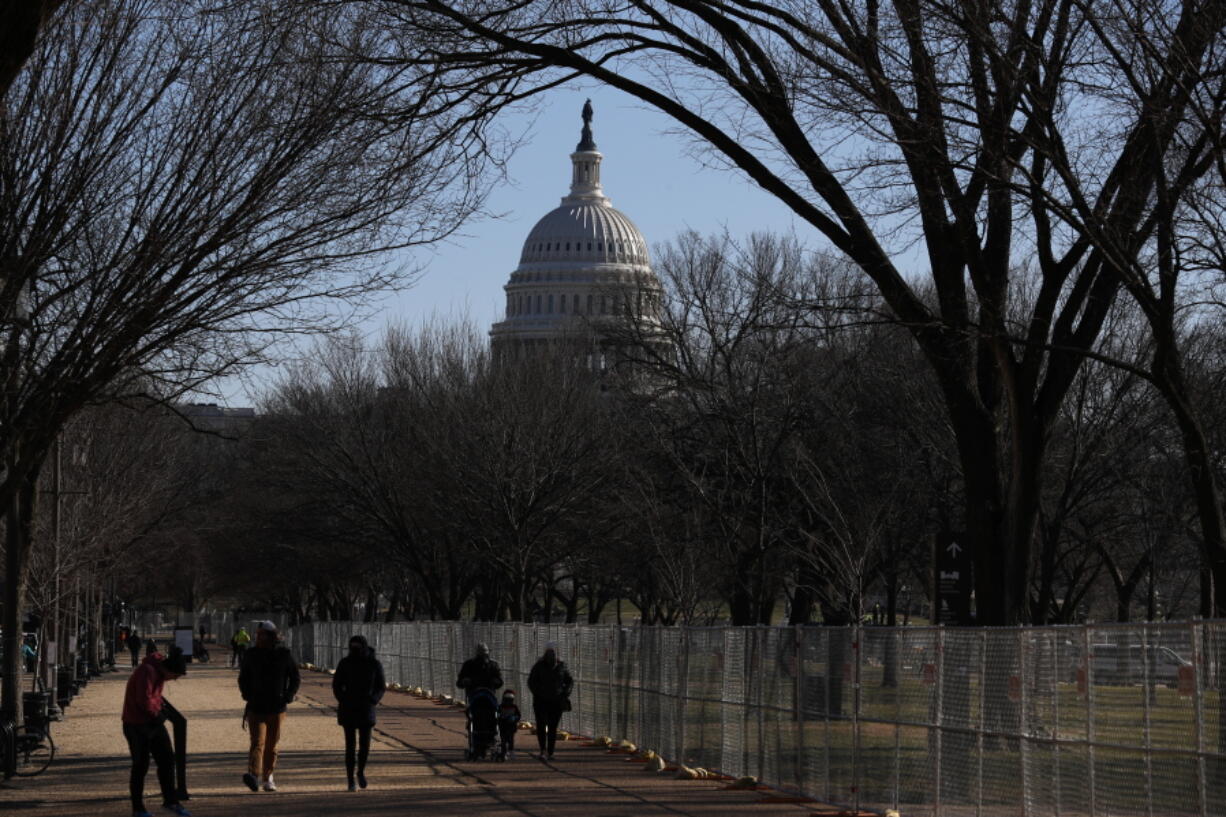 People stroll past a section of the National Mall by the Capitol where workers were still dismantling inauguration installations, after most downtown streets and public spaces had reopened to the public, on Saturday, Jan. 23, 2021 in Washington. Biden is looking to jump-start his first 100 days in office with action and symbolism to reassure a divided and weary public that help is in the offing.