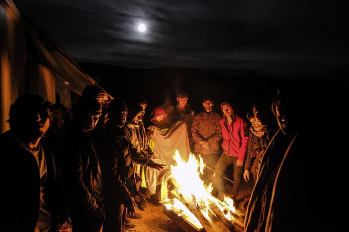 Migrants warm themselves around a fire at the Lipa camp outside Bihac, Bosnia, Wednesday, Dec. 30, 202, after hundreds failed to be relocated from the burnt-out tent camp in the northwest of the country. The migrants were supposed on Tuesday to be transferred from the much-criticized Lipa camp to a new location in the central part of the country, but have instead spent some 24 hours in buses before being told on Wednesday afternoon to disembark and return to the now empty camp site.