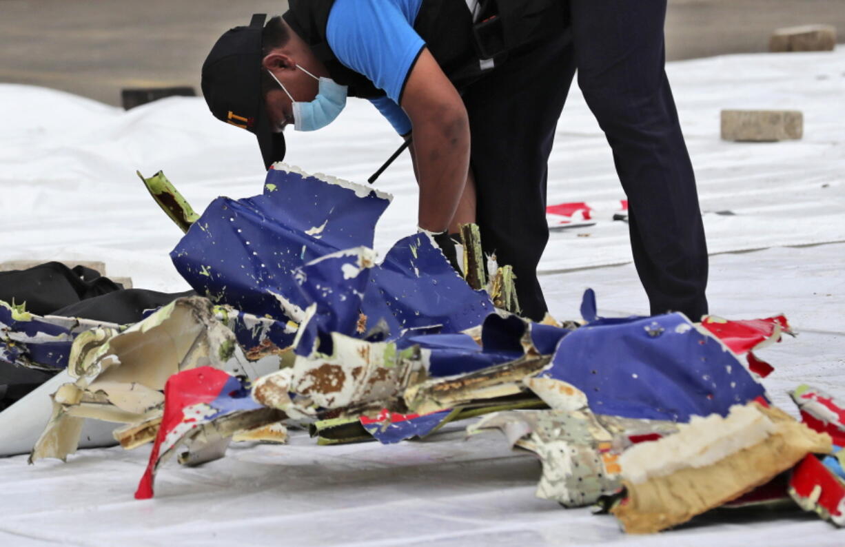 An investigator of Indonesian National Transportation Safety Committee inspects parts of Sriwijaya Air Flight 182 that crashed in the waters off Java Island, at Tanjung Priok Port in Jakarta, Indonesia, Sunday, Jan. 10, 2021. Indonesian rescuers pulled out body parts, pieces of clothing and scraps of metal from the Java Sea early Sunday morning, a day after the Boeing 737-500 with dozens of people onboard crashed shortly after takeoff from Jakarta, officials said.