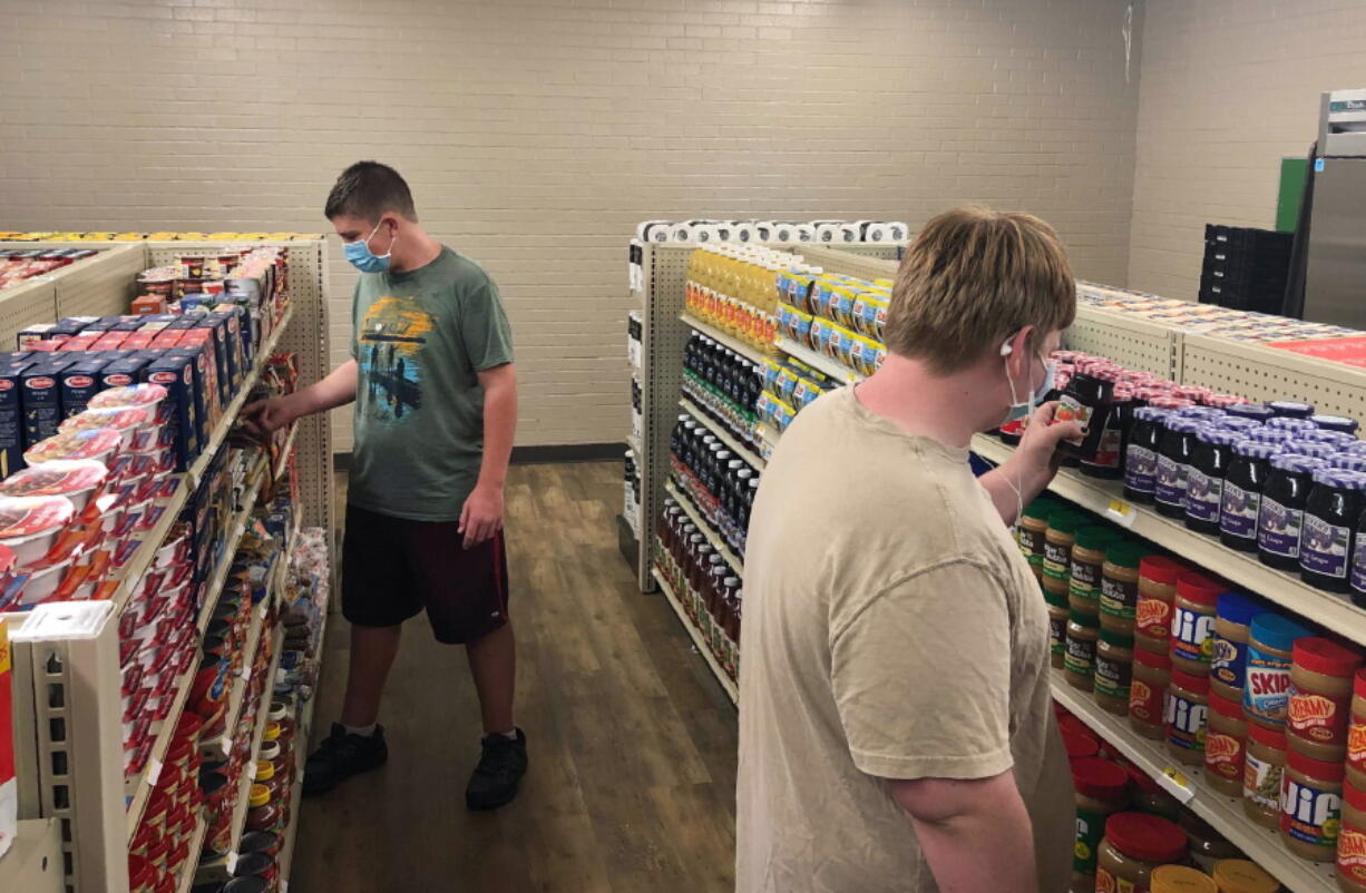 In this photo provided by Anthony Love, student Hunter Weertman, 16, left, stocks shelves and takes inventory while working as a manager of the student-led free grocery store at Linda Tutt High School on Nov. 20, 2020, in Sanger, Texas. The store provides food, toiletries and household items to students, faculty and community members in need.