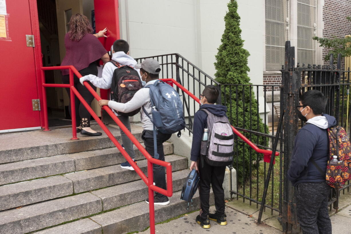 FILE - In this Sept. 29, 2020, file photo, a teacher leads her students into an elementary school in the Brooklyn borough of New York as hundreds of thousands of elementary school students are heading back to classrooms in the city, resuming in-person learning during the coronavirus pandemic. President Joe Biden says he wants most schools serving kindergarten through eighth grade to reopen by late April 2021. But even if that happens, many schools in urban areas that serve high concentrations of minority students are likely to stay closed.