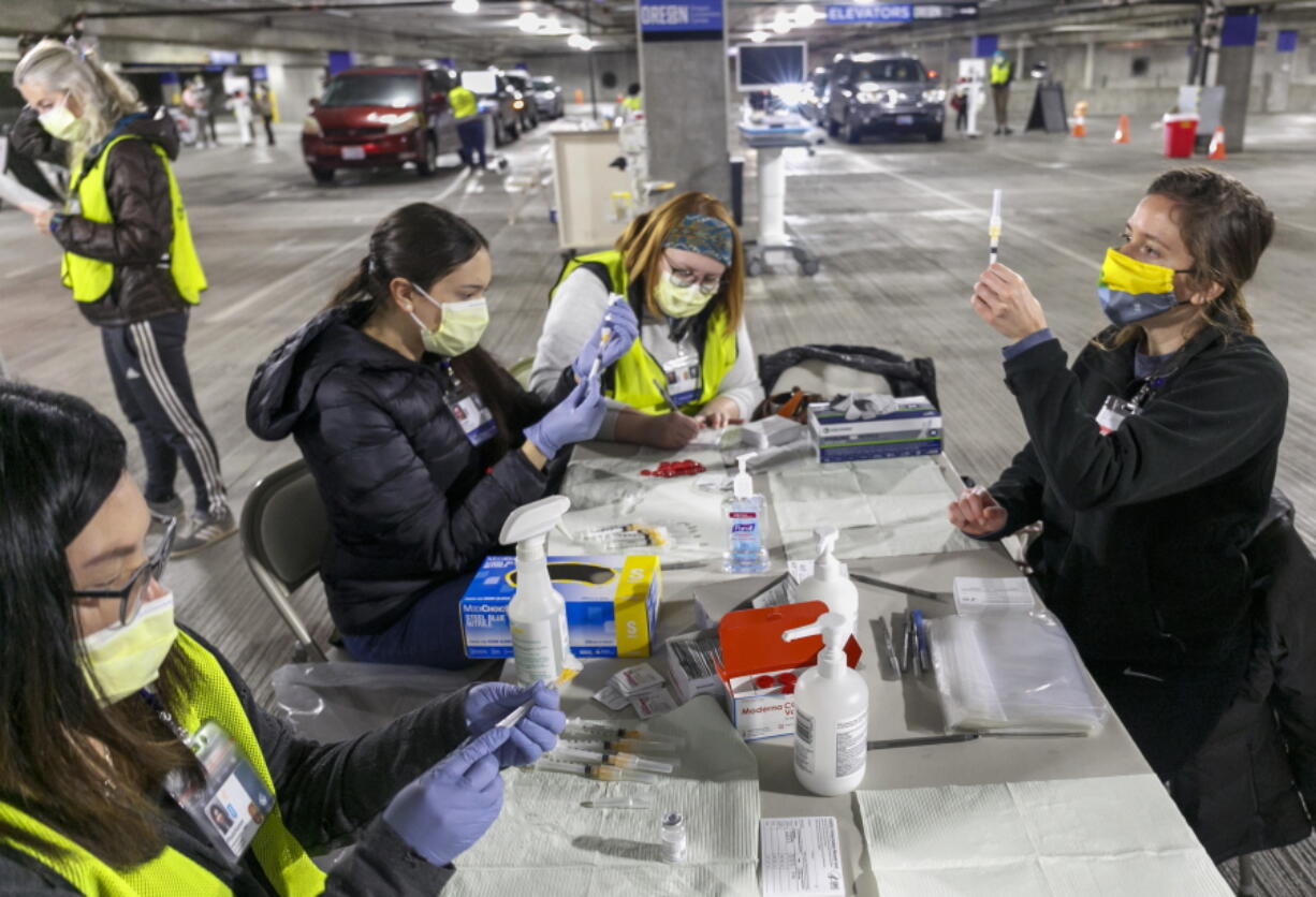 FILE - In this Sunday, Jan. 10, 2021, file photo, Medical professionals from Oregon Health &amp; Science University load syringes with the Moderna COVID-19 vaccine at a drive-thru vaccination clinic in Portland, Ore. The U.S. is entering the second month of the largest vaccination effort in history with a massive expansion of the campaign, opening up football stadiums, major league ballparks, fairgrounds and convention centers to inoculate a larger and more diverse pool of people.