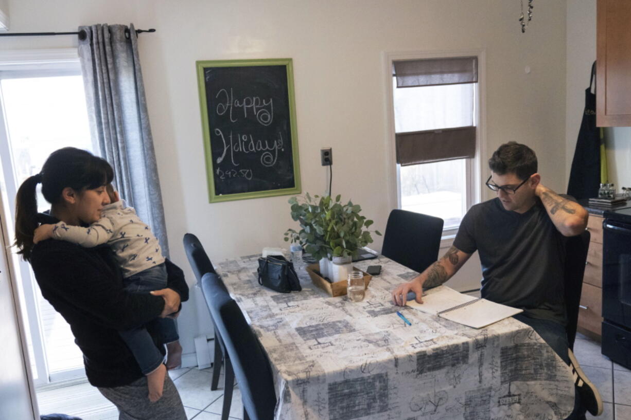 Comedian Brad Pierce, right, looks over the notebook us uses to write jokes as he sits in the kitchen next to his wife, Carmen, and their nephew, Maddox, 1, in West Warwick, R.I., Friday, Jan. 8, 2021. Pierce was finally doing well with his comedy when the pandemic hit. Now he wonders if he can possibly build up his career again. He has a friend who drives for Amazon and fears having to get a job like that while talking about the good old days when he was an entertainer.