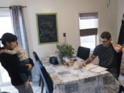 Comedian Brad Pierce, right, looks over the notebook us uses to write jokes as he sits in the kitchen next to his wife, Carmen, and their nephew, Maddox, 1, in West Warwick, R.I., Friday, Jan. 8, 2021. Pierce was finally doing well with his comedy when the pandemic hit. Now he wonders if he can possibly build up his career again. He has a friend who drives for Amazon and fears having to get a job like that while talking about the good old days when he was an entertainer.