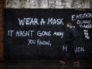 A man wearing a face covering walks past graffiti on the Lower Newtownards Road in Belfast with a message reading &#039;Wear a mask, it hasn&#039;t gone away you know&#039; Friday, Jan. 1, 2021.