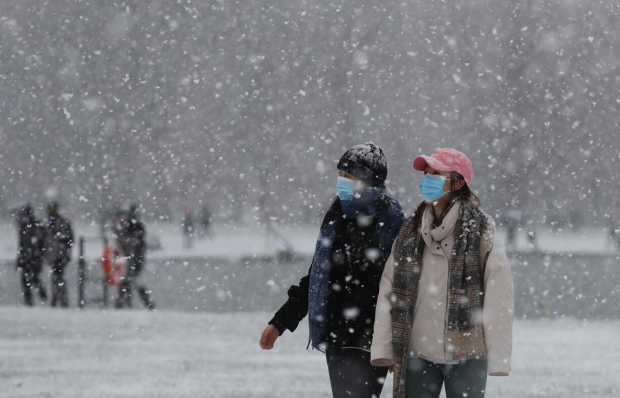 Pedestrians wearing face masks against the coronavirus pandemic walk in Kensington Gardens as snow falls in London, Sunday, Jan. 24, 2021.