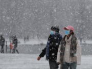 Pedestrians wearing face masks against the coronavirus pandemic walk in Kensington Gardens as snow falls in London, Sunday, Jan. 24, 2021.