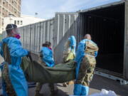 FILE - In this Jan. 12, 2021 photo provided by the Los Angeles County Department of Medical Examiner-Coroner, National Guard members assisting with processing COVID-19 deaths, placing them into temporary storage at the medical examiner-coroner&#039;s office in Los Angeles. The seven-day rolling average of daily deaths is rising in 30 states and the District of Columbia, and on Monday, Jan 18, 2021, the U.S. was approaching 398,000, according to data collected by Johns Hopkins University, by far the highest of any country in the world.