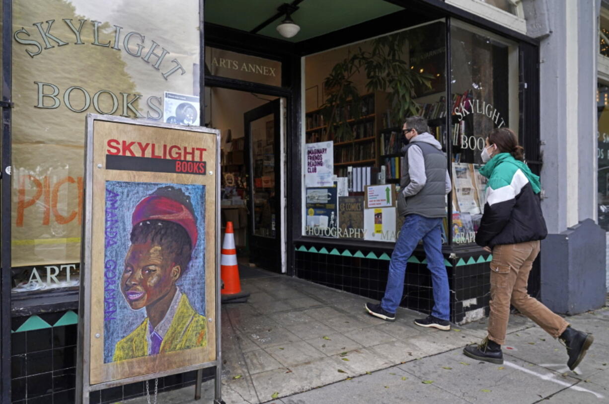 Eric and Tess from Pasadena, Calif., enter the Skylight Book store, decorated with a poster of American poet Amanda Gorman, in Los Feliz neighborhood of Los Angeles Monday, Jan. 25, 2021. California has lifted regional stay-at-home orders statewide in response to improving coronavirus conditions. Public health officials said Monday that the state will return to a system of county-by-county restrictions intended to stem the spread of the virus. Local officials could choose to continue stricter rules. The state is also lifting a 10 p.m. to 5 a.m. curfew.