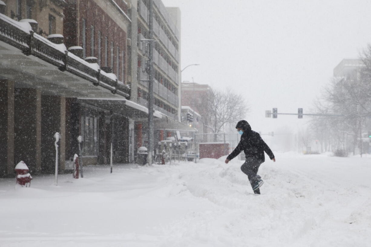 A pedestrian steps in tire tracks while crossing the street during a winter storm in downtown Lincoln, Neb. on Monday, Jan. 25, 2021.