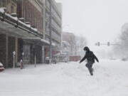 A pedestrian steps in tire tracks while crossing the street during a winter storm in downtown Lincoln, Neb. on Monday, Jan. 25, 2021.