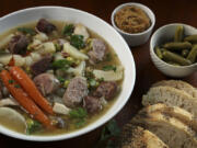 Pot au feu (boiled meats dinner) is served with accompaniments like carrots, pearl onions, fresh herbs, pickles, mustard.