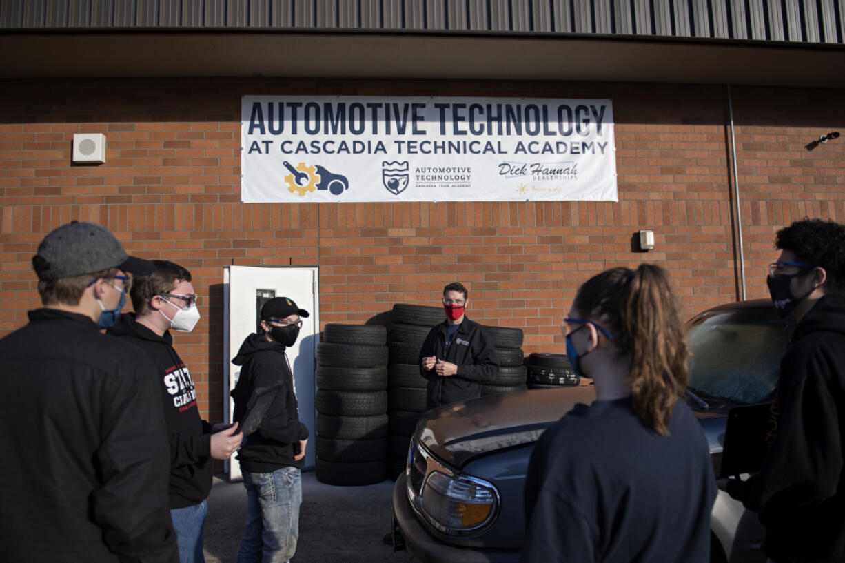 Automotive instructor Adam Eldridge, center in red mask, works with students as they prepare to push a car inside the auto shop at Cascadia Tech Academy. Remote learning has been a challenge for students learning hands-on occupations.