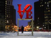 A person wearing a face mask as a precaution against the coronavirus walks during a winter storm near the Robert Indiana sculpture &quot;LOVE&quot; at John F. Kennedy Plaza, commonly known as Love Park, in Philadelphia, Monday, Feb. 1, 2021.