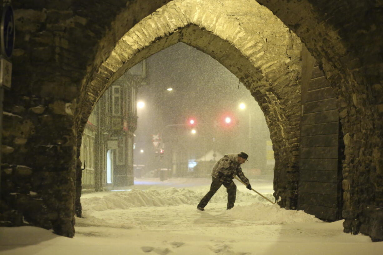 A resident shovels snow under an archway in Wernigerode, Germany, early Sunday morning, Feb. 7, 2021. Low Tristan has caused huge amounts of snow in the Harz mountains, like here in Wernigerode.