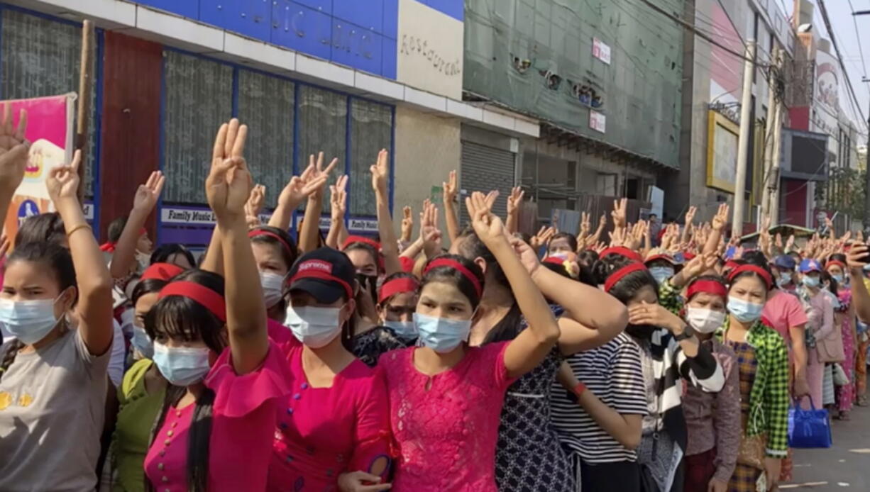 In this image made from video, protesters flash the three-fingered salute while they gather to march Saturday in Yangon, Myanmar.