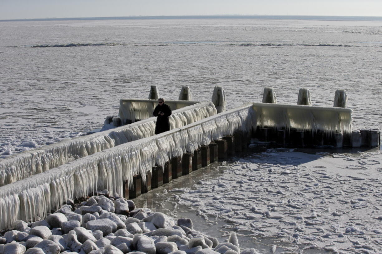 A woman takes pictures of icicles on a jetty at the Afsluitdijk, a dike separating IJsselmeer inland sea, and the Wadden Sea, Netherlands, Thursday, Feb. 11, 2021. The deep freeze gripping parts of Europe served up fun and frustration with heavy snow cutting power to some 37,000 homes in central Slovakia.