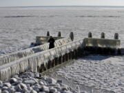 A woman takes pictures of icicles on a jetty at the Afsluitdijk, a dike separating IJsselmeer inland sea, and the Wadden Sea, Netherlands, Thursday, Feb. 11, 2021. The deep freeze gripping parts of Europe served up fun and frustration with heavy snow cutting power to some 37,000 homes in central Slovakia.