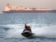 FILE - In this Friday, July 26, 2019 file photo, a ship crosses the Gulf of Suez towards the Red Sea as holiday-makers ride a jet ski at al Sokhna beach in Suez, 127 kilometers (79 miles) east of Cairo, Egypt. Not only are humans changing the surface and temperature of the planet, but also its sounds - and those shifts are detectable even in the open ocean, according to research published Thursday, Feb. 4, 2021.