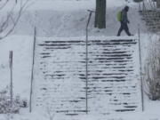 A pedestrian walks near a snow-covered staircase, Saturday, Feb. 13, 2021, on the University of Washington campus in Seattle. Winter weather was expected to continue through the weekend in the region.(AP Photo/Ted S.