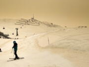 Skiers wearing protective face mask ski as Sahara sand colours the snow and the sky in orange and creates a special light atmosphere, during the coronavirus disease (COVID-19) outbreak, in the Alpine resort of Anzere, Switzerland, on Saturday, 6 February 2021.