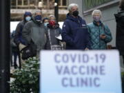 FILE - In this an. 24, 2021, file photo, people stand near a sign as they wait in line to receive the first of two doses of the Pfizer vaccine for COVID-19 at a one-day vaccination clinic set up in an Amazon.com facility in Seattle and operated by Virginia Mason Franciscan Health. Scientists say it&#039;s still too early to predict the future of the coronavirus, but many doubt it will ever go away entirely. (AP Photo/Ted S.