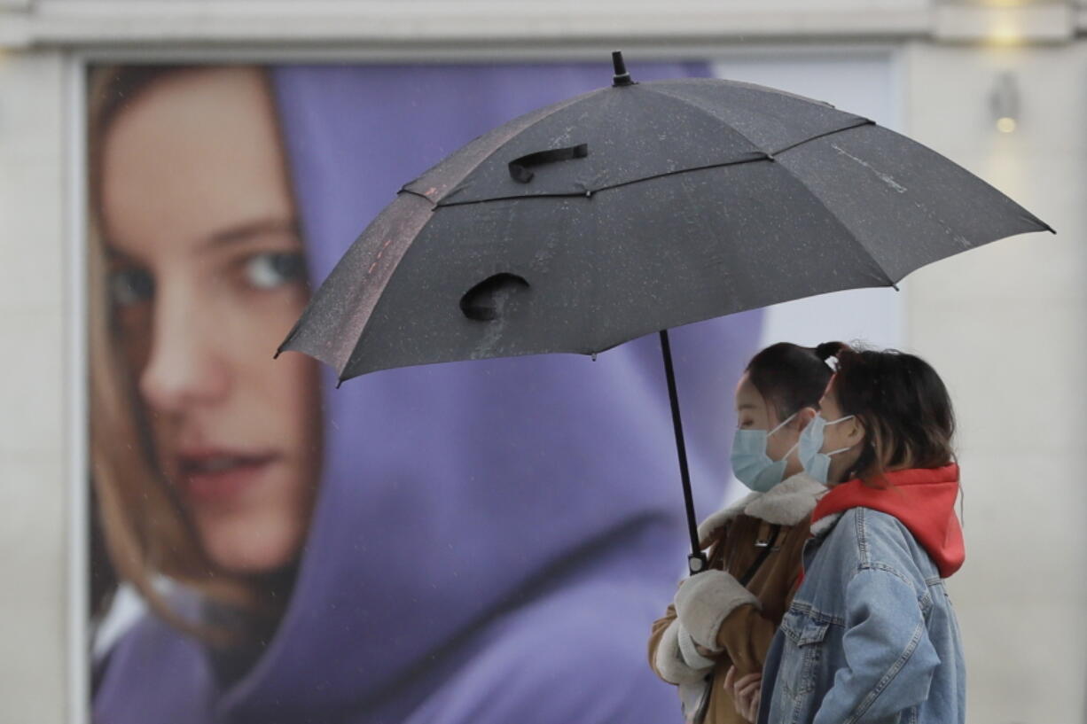 People wear masks to protect against coronavirus as they pass a shop in London, Wednesday, Feb. 3, 2021. Britain&#039;s Health Secretary Matt Hancock said Wednesday a new study suggesting that a single dose of the AstraZeneca vaccine may reduce transmission of COVID-19 categorically supports the government&#039;s strategy of taking more time between injections.