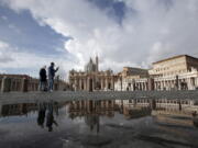 FILE - In this Sunday, Jan. 31, 2021 file photo, people are reflected on a puddle as they walk in St. Peter&#039;s Square, at the Vatican. The Vatican is taking Pope Francis&#039; pro-vaccine stance very seriously: Any Vatican employee who refuses to get a coronavirus shot without valid medical reason risks being fired.